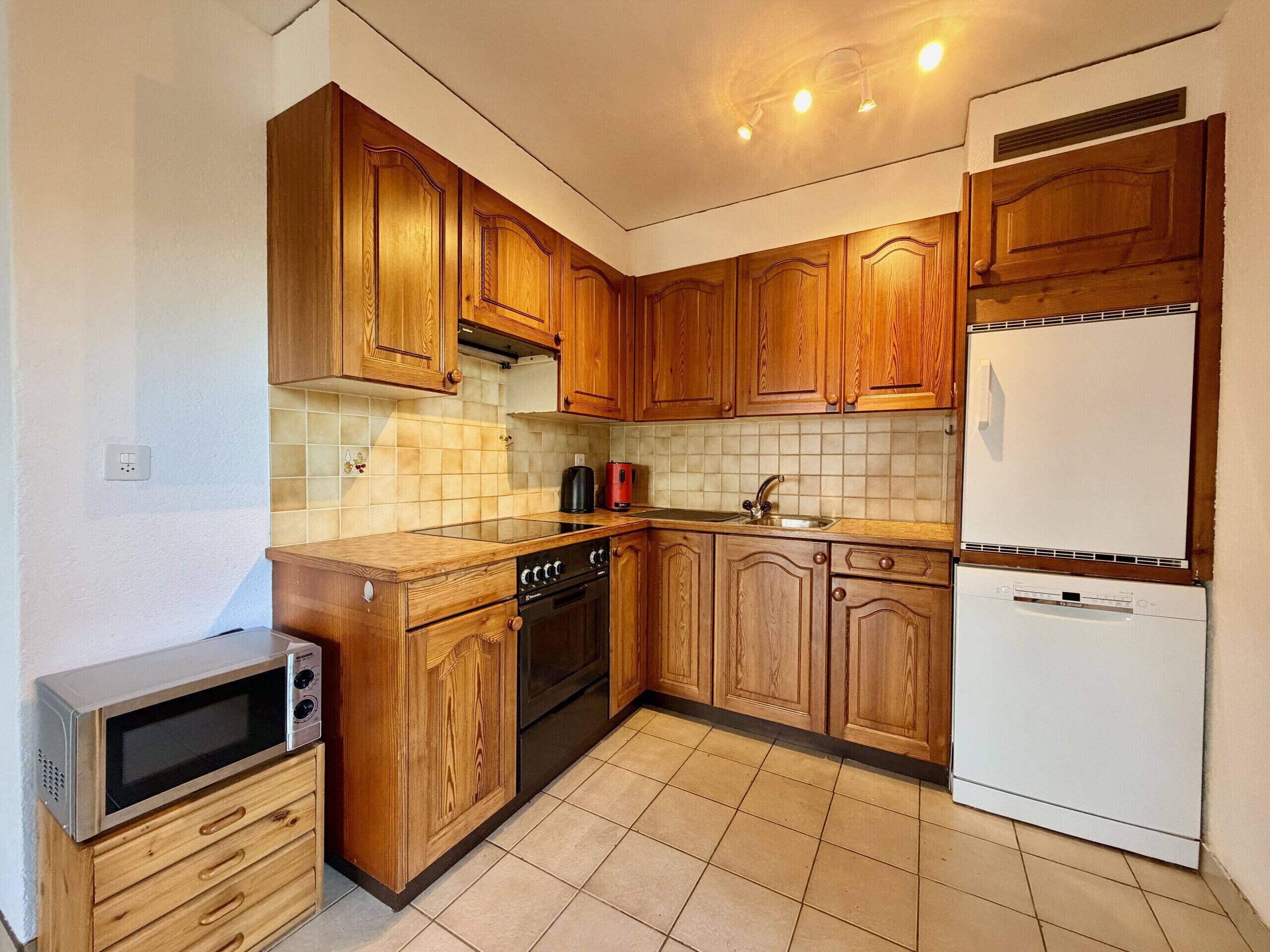 Een keuken met houten kastjes, een magnetron, een fornuis, een spoelbak en een koelkast.