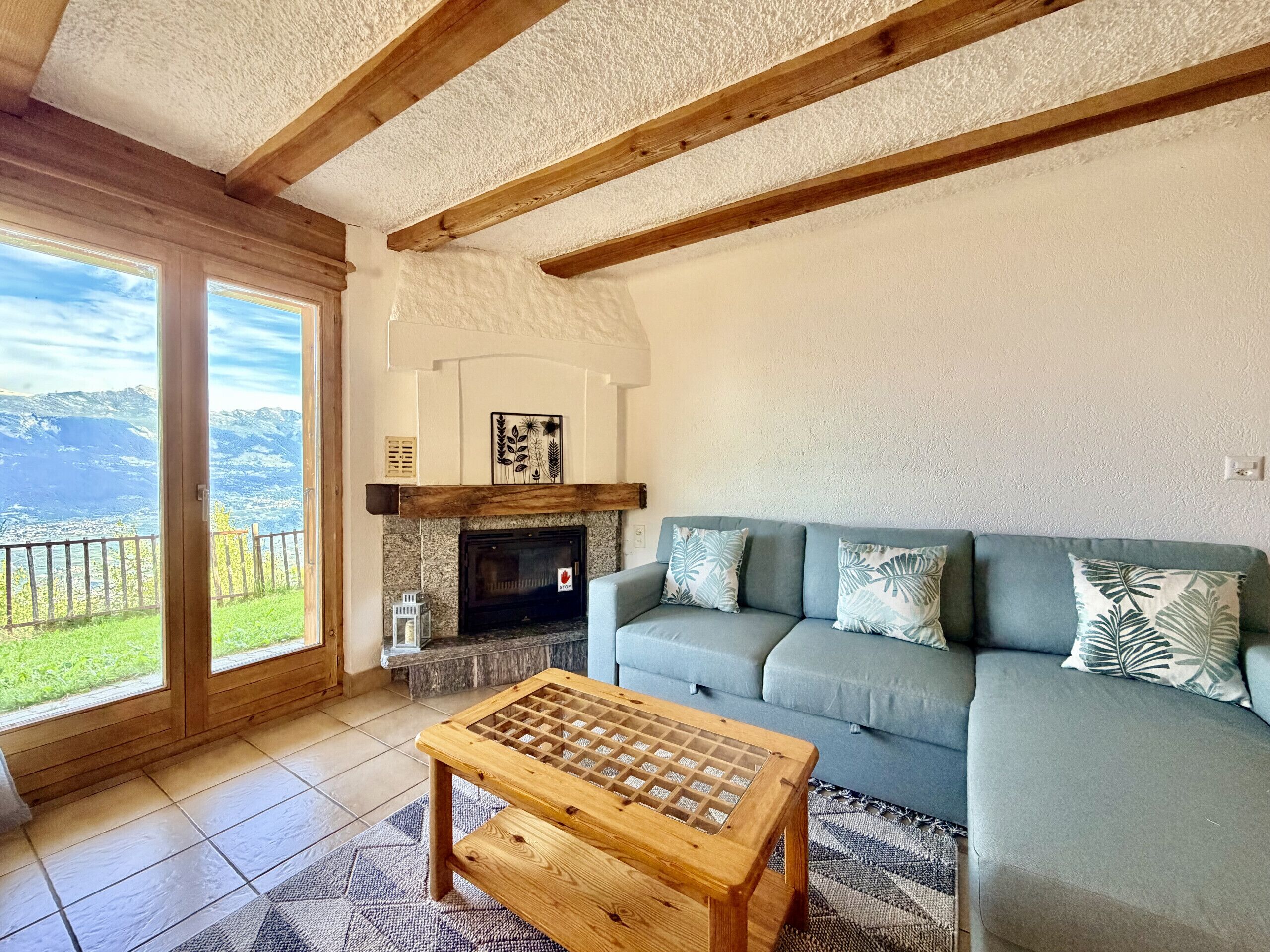 Una sala de estar con chimenea, un sofá, una mesa de centro de madera y vistas a montañas a través de amplios ventanales.