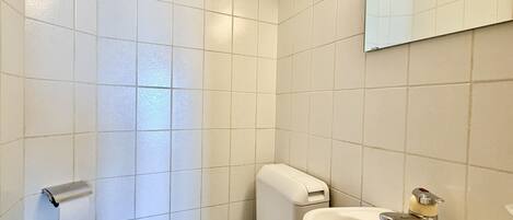 A bathroom with white tiles, a toilet, a sink, and a mirror.