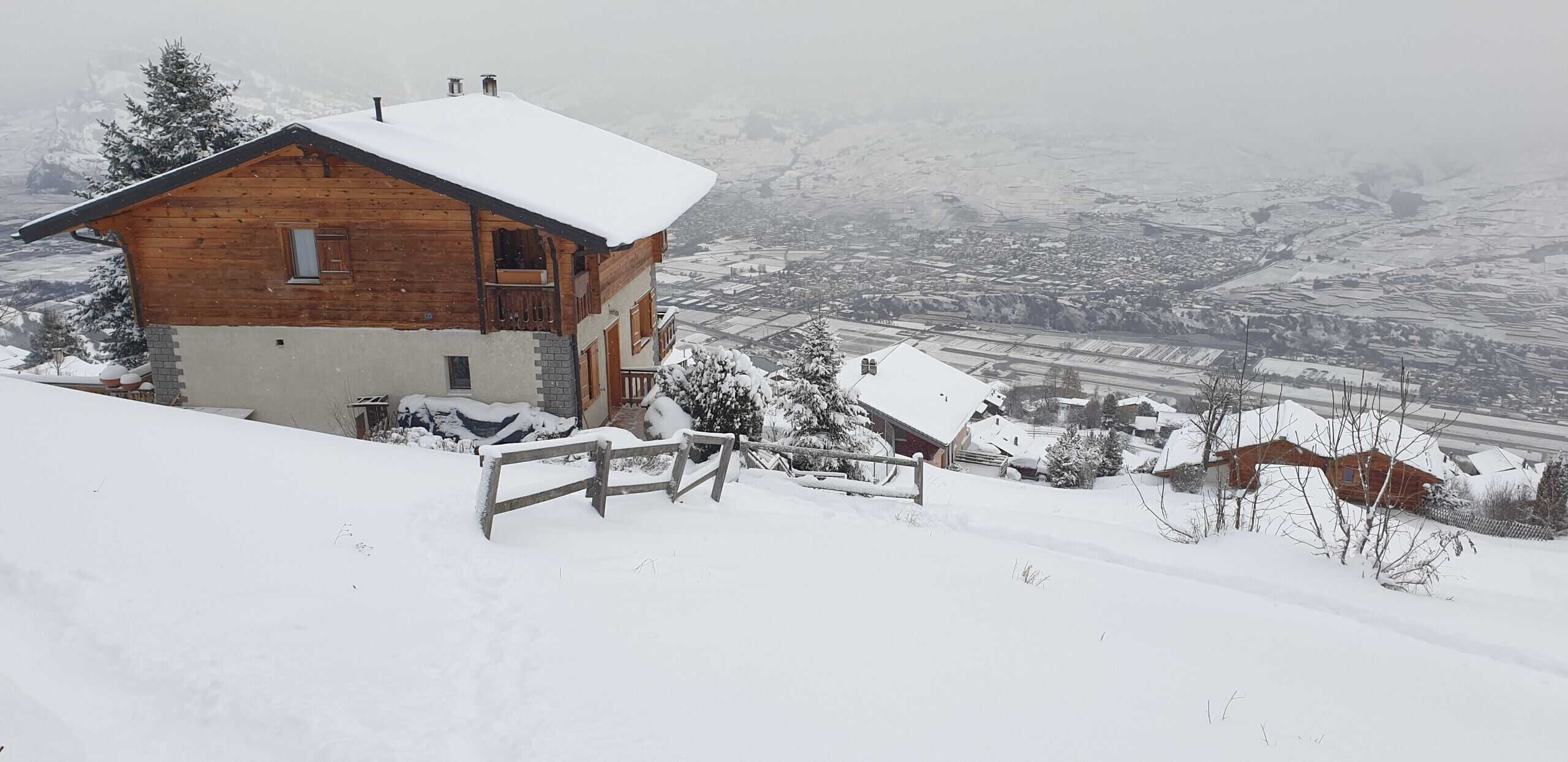 Een houten chalet met sneeuw op het dak, een balkon en uitzicht op een besneeud dal.