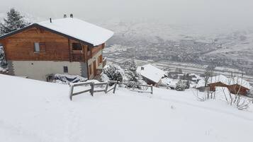 Een houten chalet met sneeuw op het dak, een balkon en uitzicht op een besneeud dal.