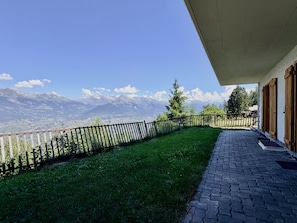 Un balcón con vistas a monta ñas, una valla de madera y un camino empedrado.