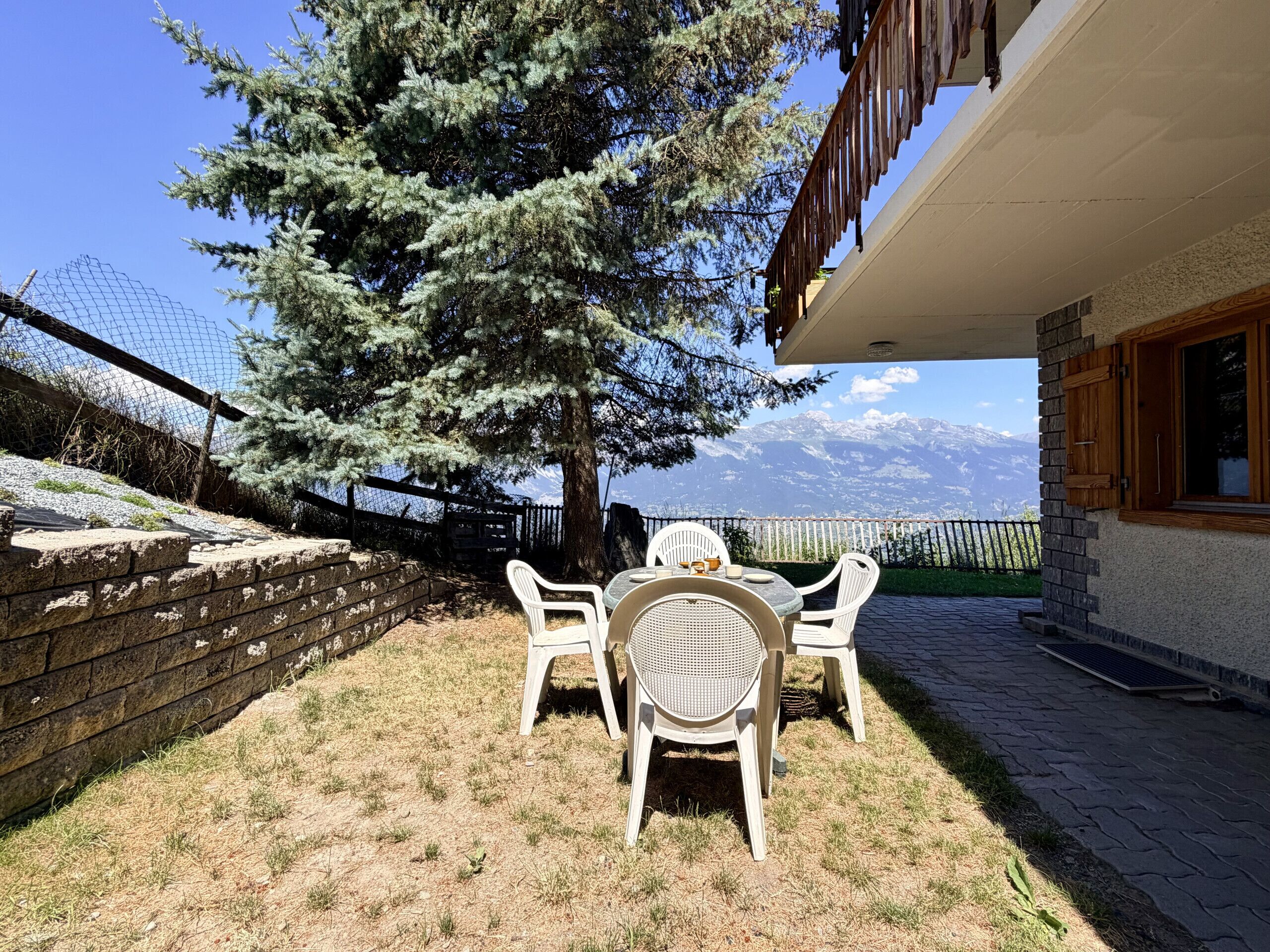 A patio with a table and chairs, a tree, and a mountain view.