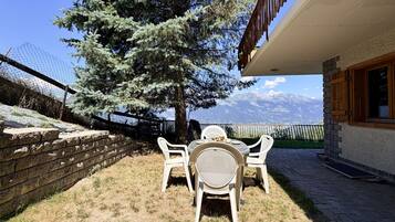 A patio with a table and chairs, a tree, and a mountain view.