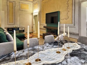 A room with a fireplace, a television mounted on the wall, and a dining table with candles. - Residenza DuLà - Two Bedroom Apartment, Sleeps 6 (Arezzo)
