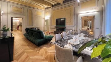 Un ampio soggiorno con un divano verde, un tavolo da pranzo per sei persone e una televisione a parete.