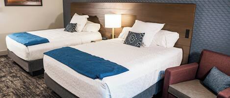 A hotel room with two beds, a nightstand with a lamp, a red armchair, and a textured wall.