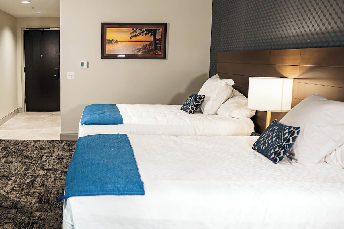 A hotel room with two beds, a framed picture on the wall, a door, and a patterned carpet.