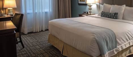 Una habitación de hotel con una cama grande, un escritorio con lámpara, una silla y una ventana con cortinas.