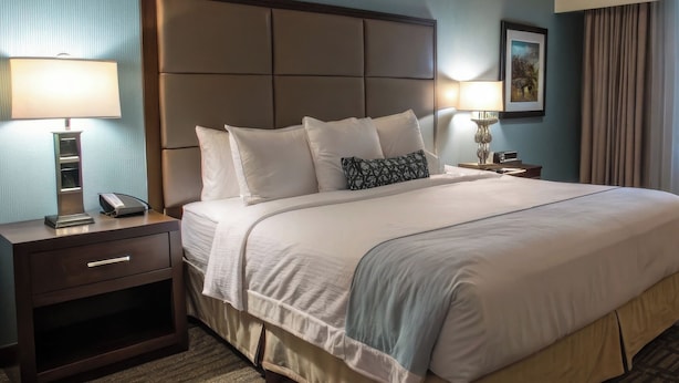 Una habitación de hotel con una cama grande, dos mesitas de noche, una lámpara y un cuadro en la pared.