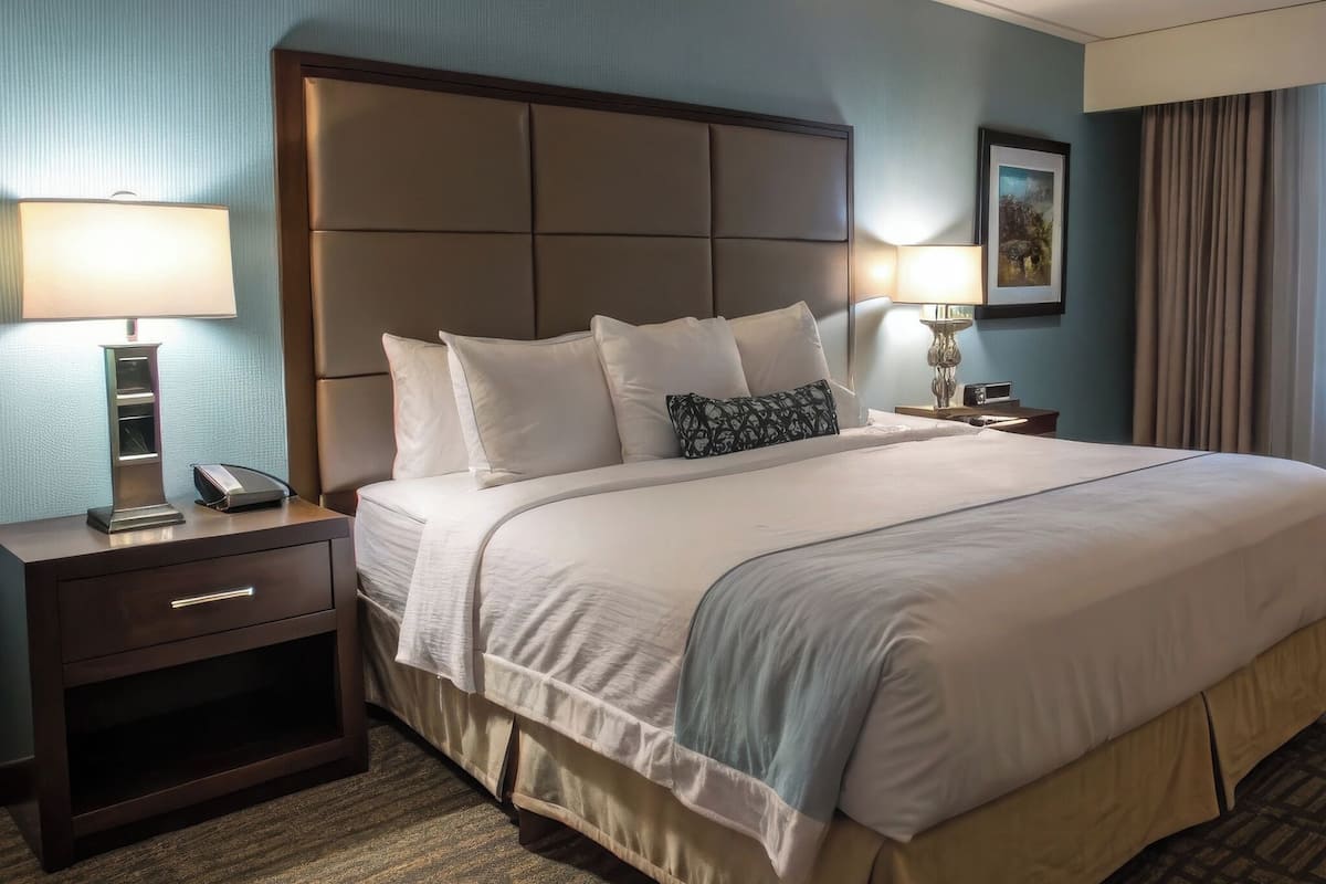 A hotel room with a large bed, two bedside tables, a nightstand, a lamp, and a framed picture on the wall.