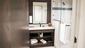 Un baño moderno con lavamanos de mármol, un espejo grande, cabina de ducha con mampara de vidrio y toallas impecablemente dobladas.