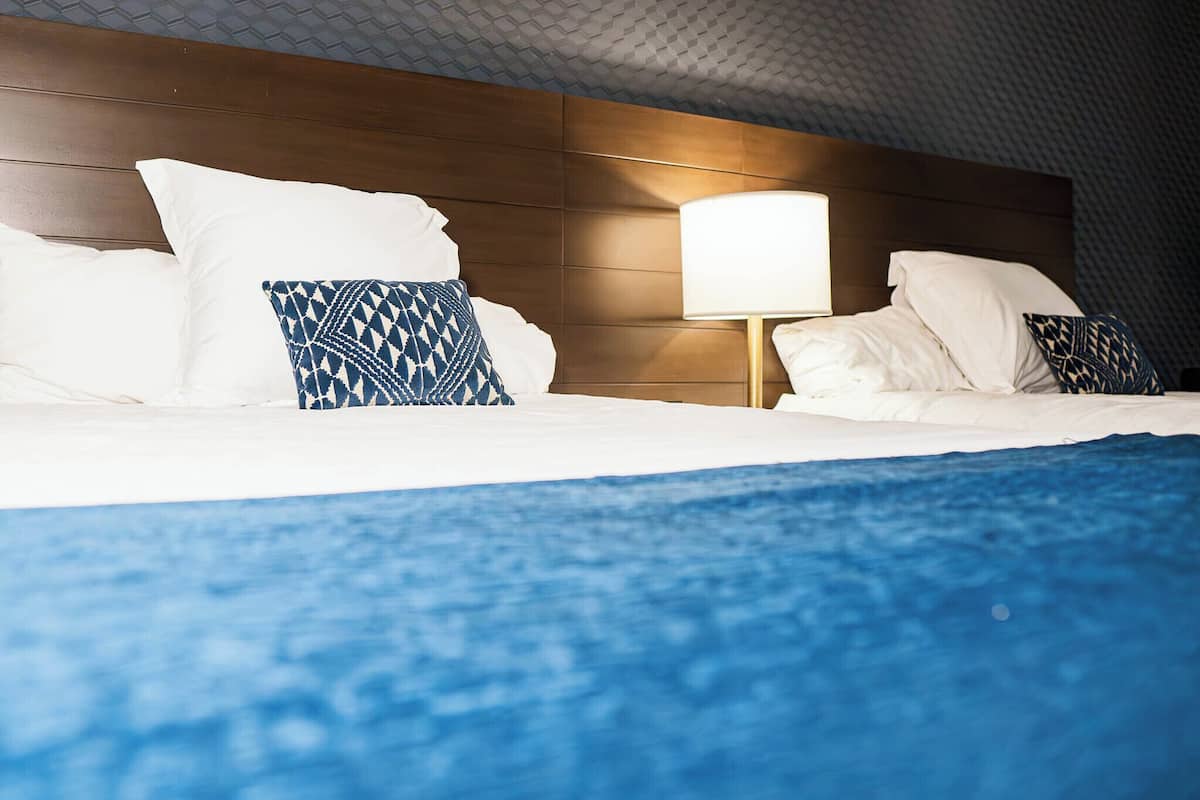 A hotel room with a wooden headboard, white bedding, and patterned pillows.