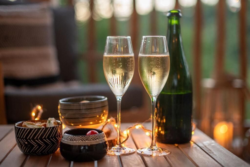 Deux coupes de champagne et une bouteille sur une table en bois, agrémentée de bols décoratifs et d’une guirlande lumineuse.