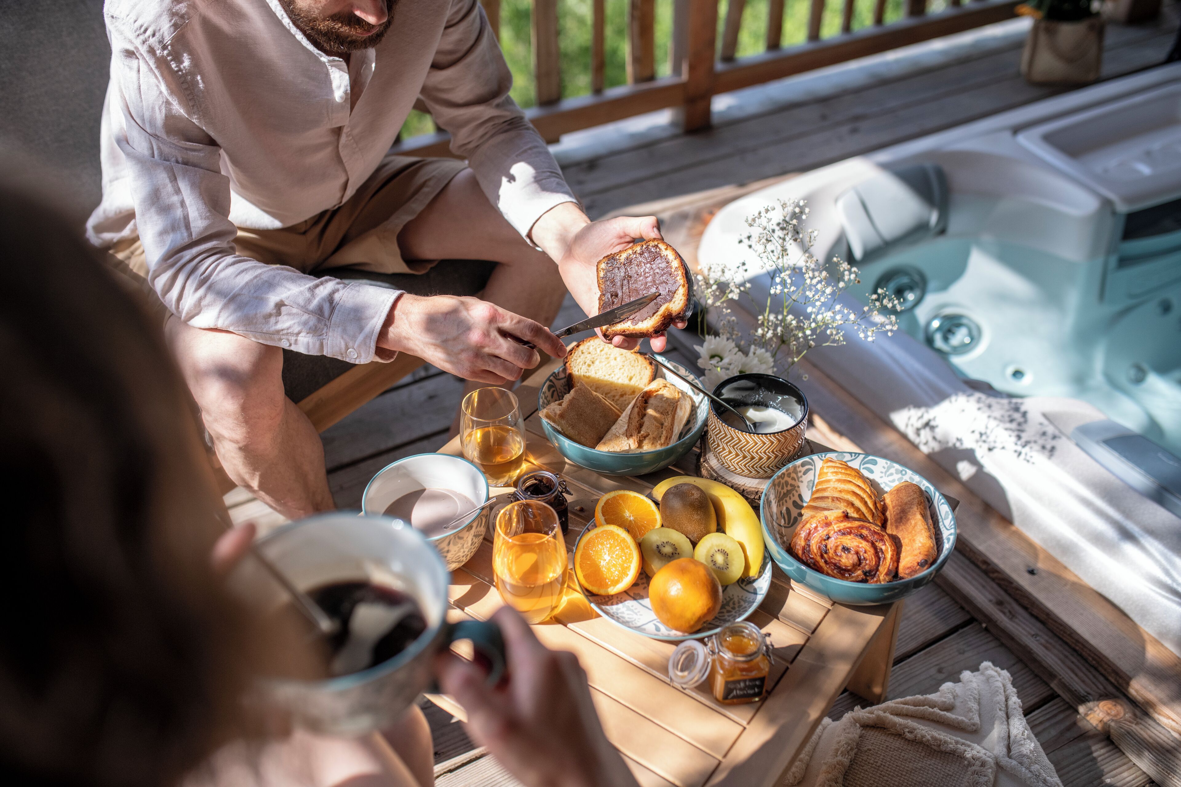 Un desayuno con pan, frutas y bebidas sobre una mesa de madera cerca de un jacuzzi.