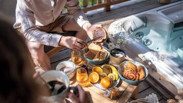 Un desayuno con pan, frutas y bebidas sobre una mesa de madera cerca de un jacuzzi.