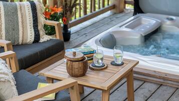 Une terrasse en bois avec un canapé, un jacuzzi et une table avec des verres et un livre.