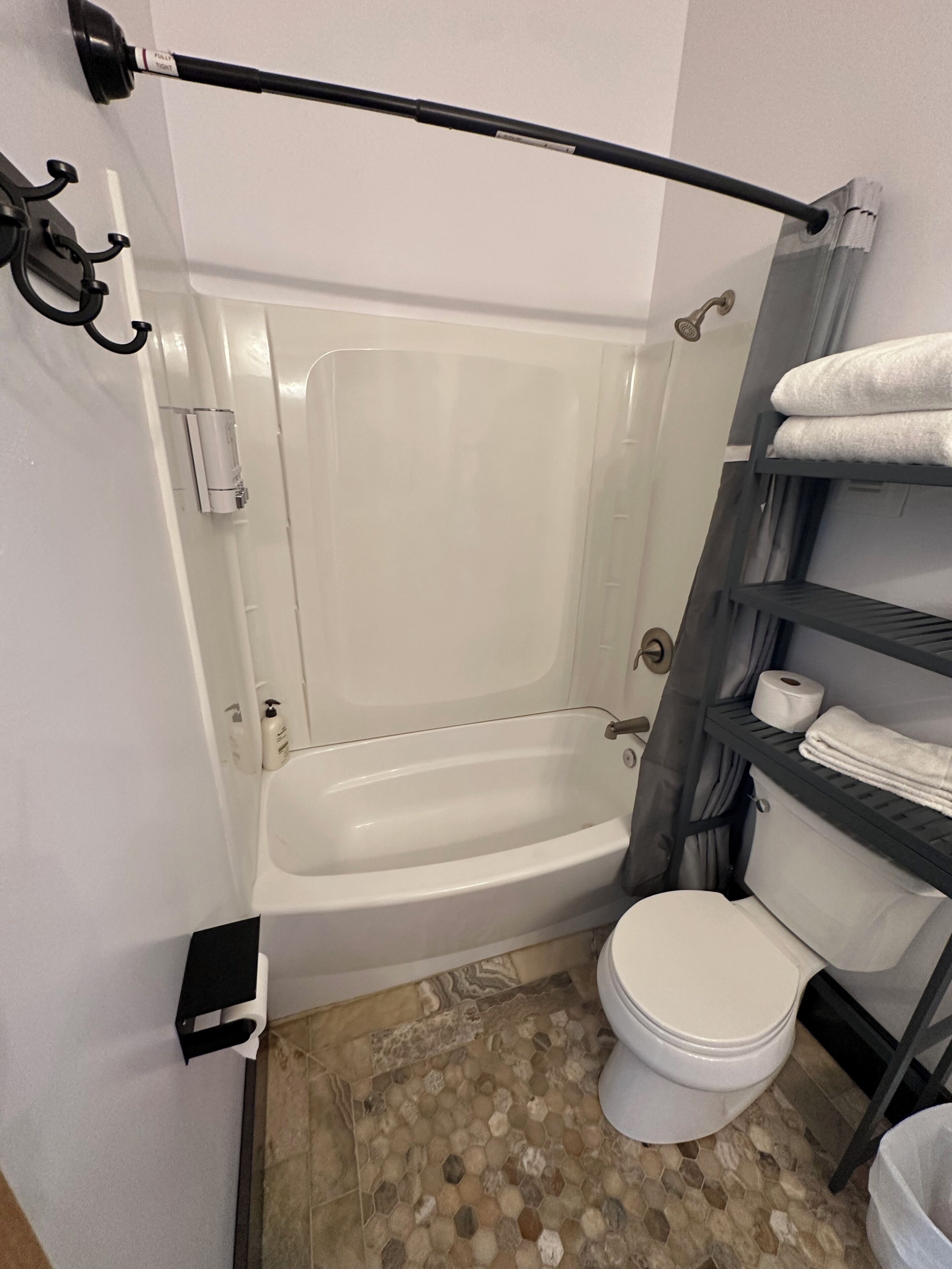 Un baño con bañera, inodoro y estantes con toallas.