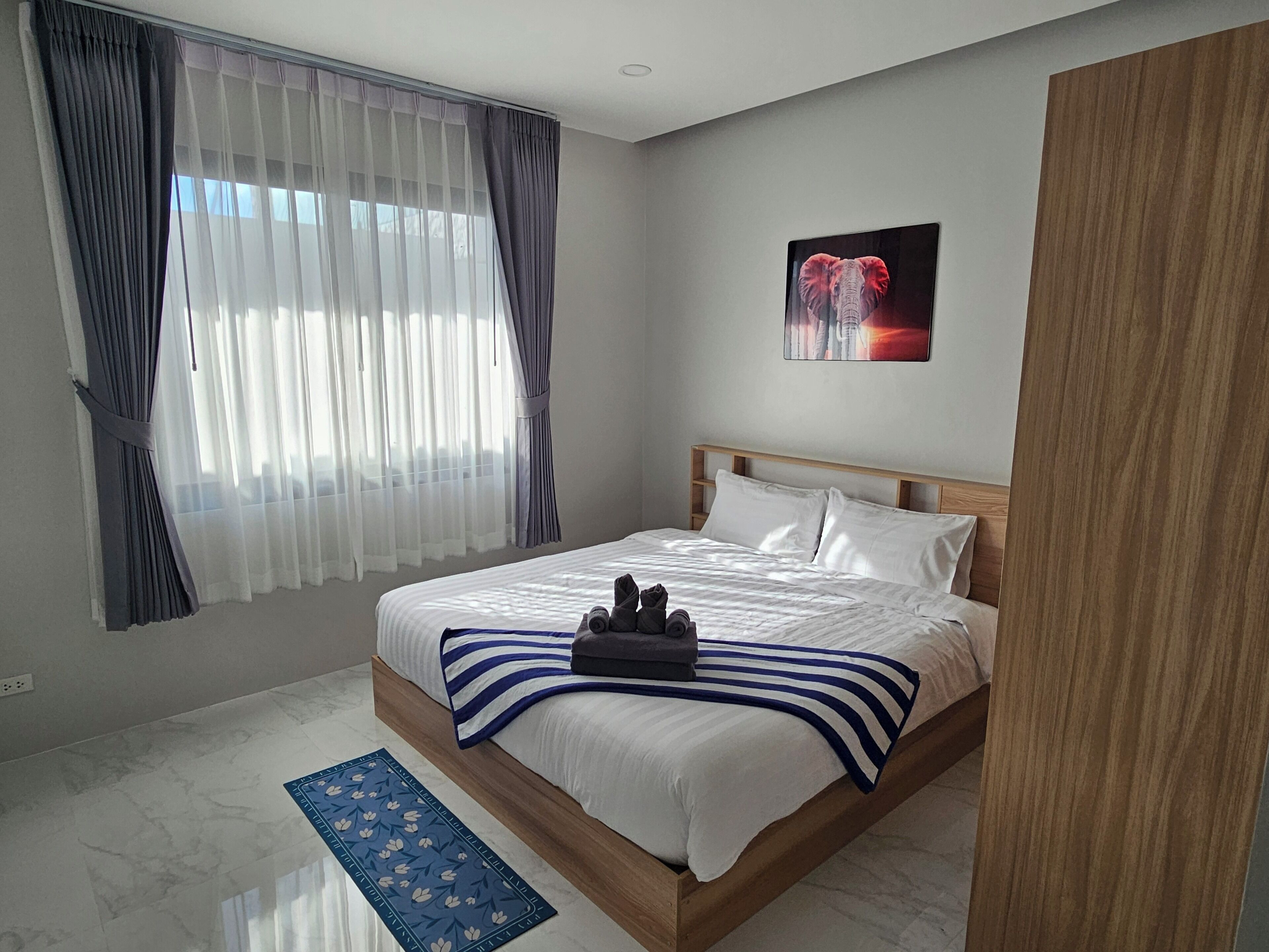 Habitación de hotel con una cama grande, un tapete azul estampado, un cabecero de madera y un cuadro de un elefante en la pared.