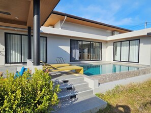Une maison moderne dotée d’une piscine, de grandes fenêtres et d’un patio couvert.