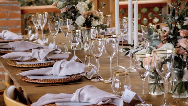 Ein Holztisch draußen gedeckt mit Gläsern, Kerzen und Blumenarrangements.