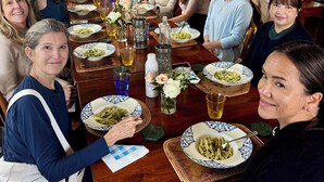 Eine Gruppe von Personen sitzt an einem Holztisch, gedeckt mit Speisen, Gläsern und einer Blumenvase.