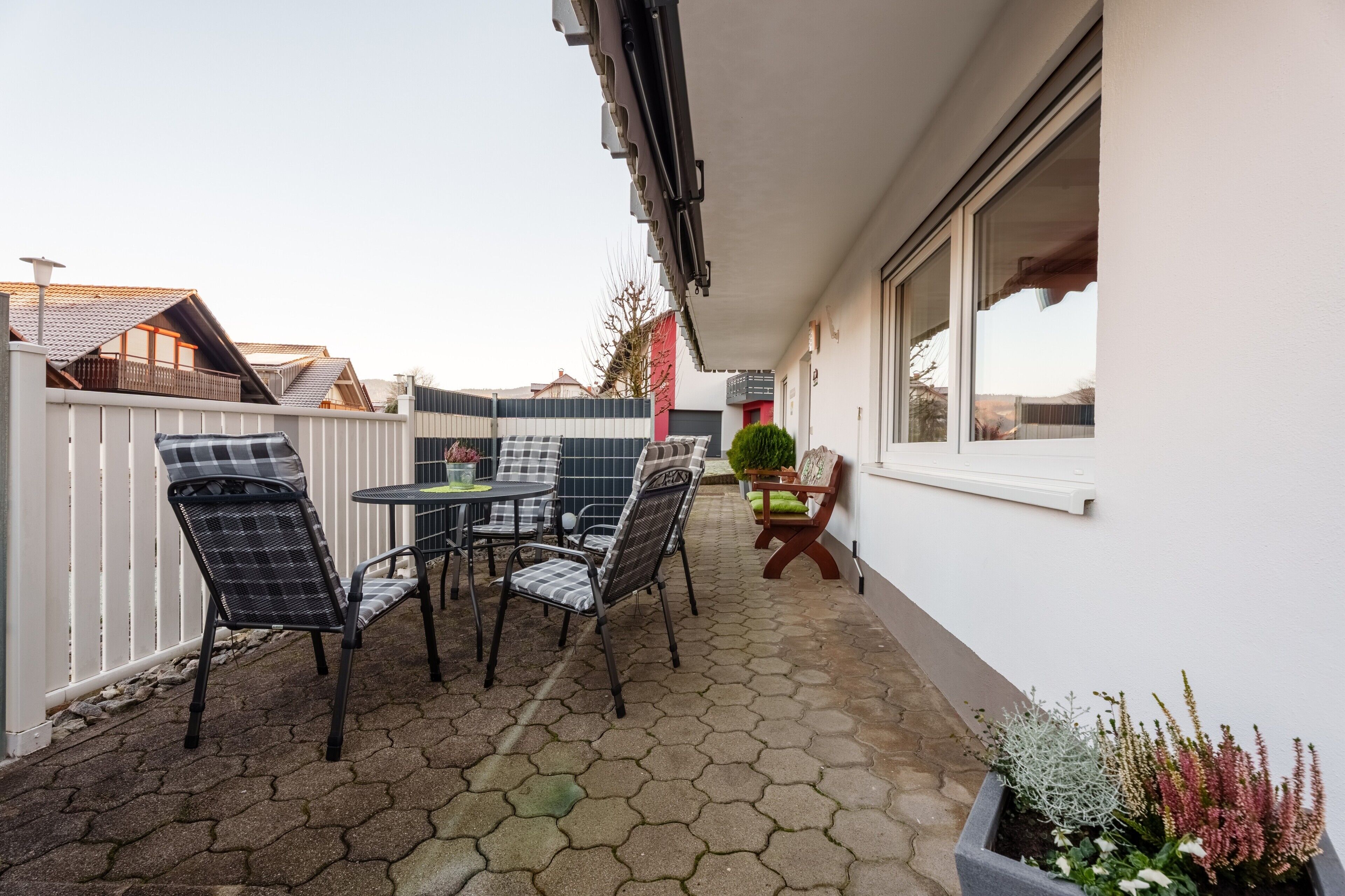 Un patio exterior con baldosas hexagonales, una mesa con sillas y plantas en macetas.