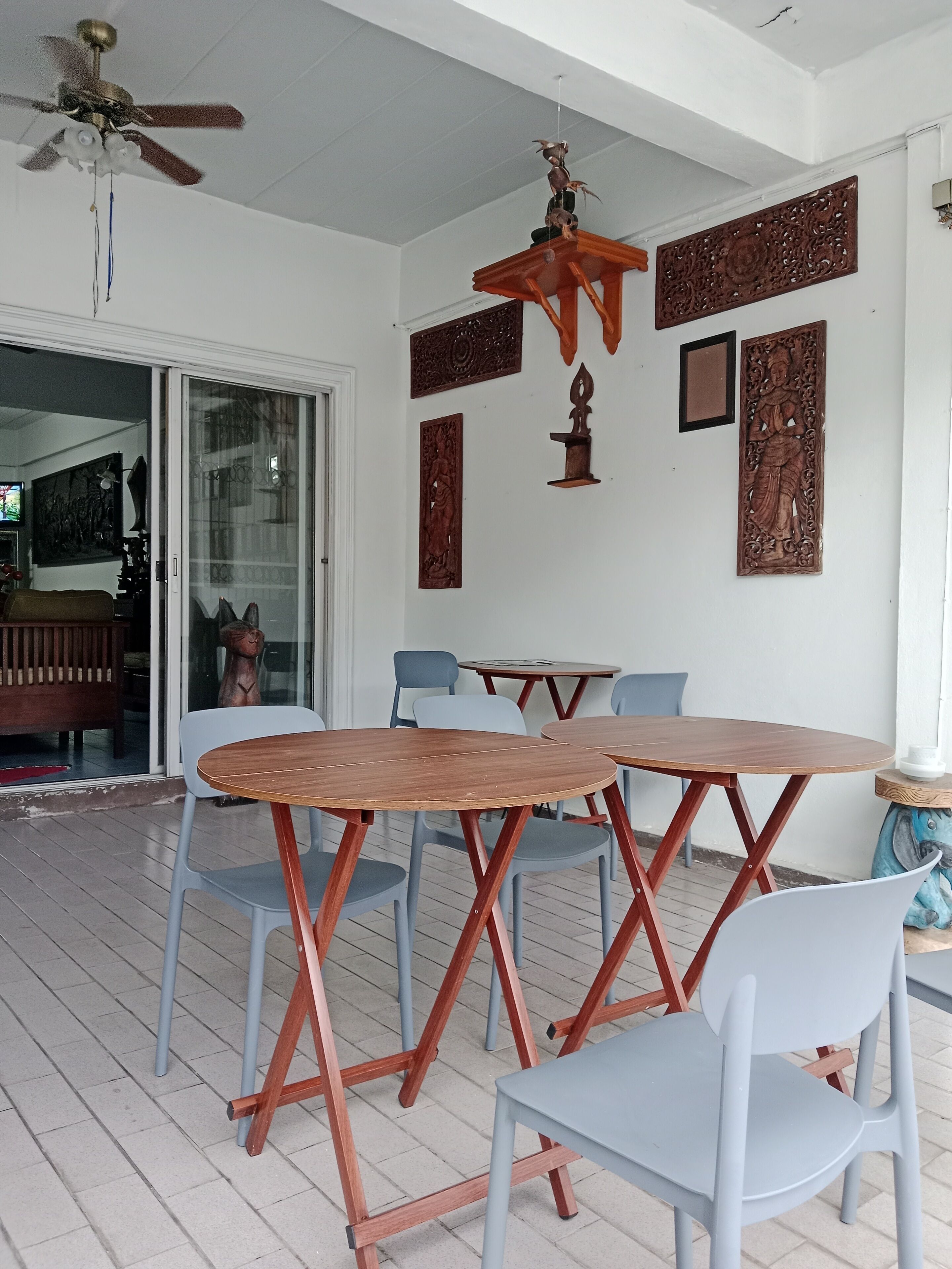 Un espace extérieur abrité, aménagé pour les repas, avec une table et des chaises en bois, des éléments décoratifs sur les murs et un ventilateur de plafond.