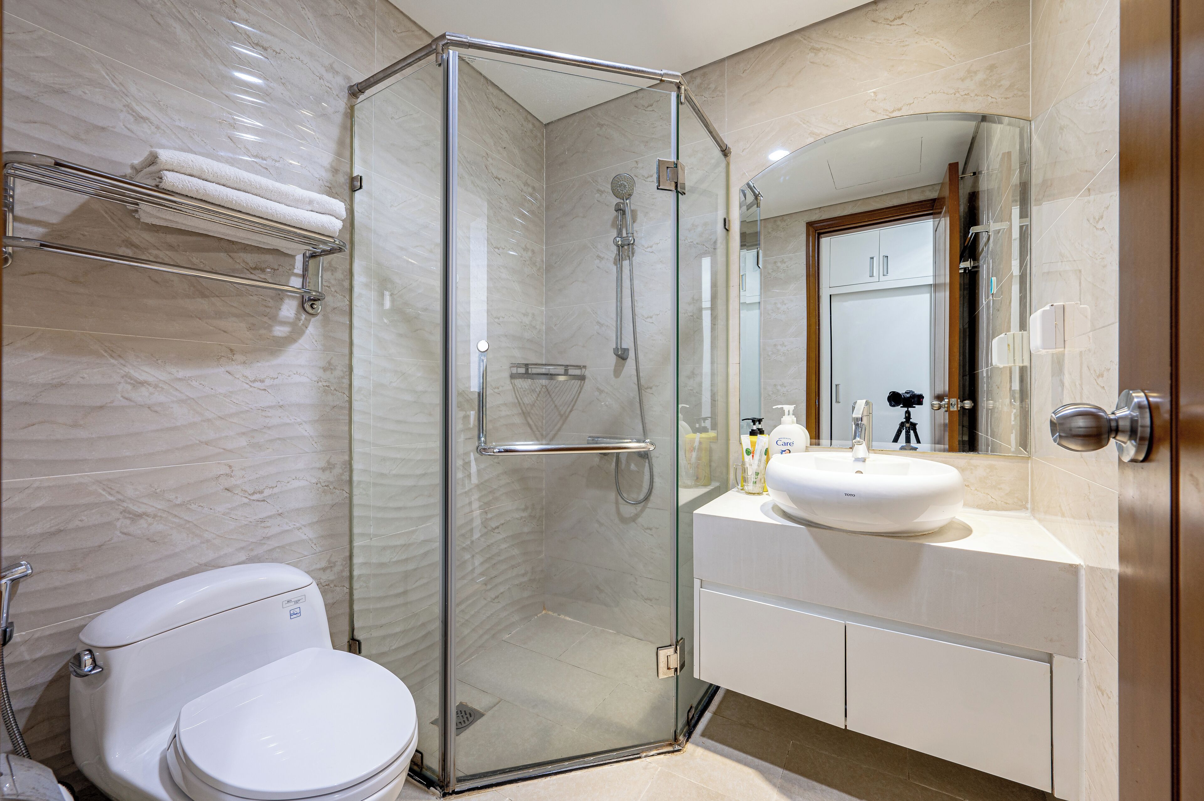 A modern bathroom with a glass-enclosed shower, a white toilet, and a sink with a mirror above it.
