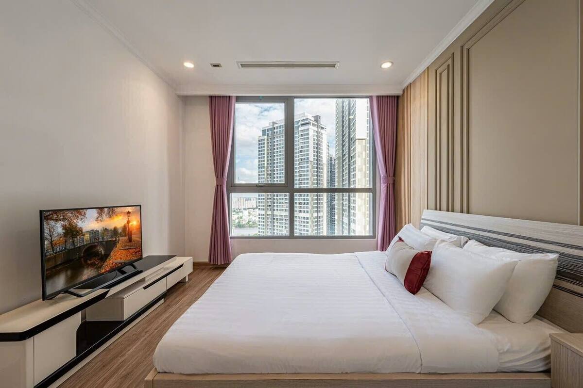 Ein modernes Hotelzimmer mit einem großen Bett, einem Flachbildfernseher auf einem Schrank und Blick auf hohe Gebäude durch das Fenster.