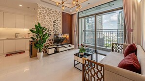 A modern living room with a sofa, TV, and a balcony with a view of the city. - Horizon Panorama Apartment Vinhomes  (Ho Chi Minh City)