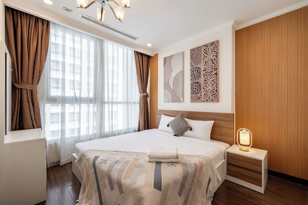 Ein Hotelzimmer mit einem großen Bett, einem Nachttisch mit Lampe, einem Fenster mit Vorhängen und einer Holzwandverkleidung.