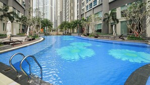 A swimming pool surrounded by high-rise buildings, palm trees, and lounge chairs. - Horizon Panorama Apartment Vinhomes  (Ho Chi Minh City)