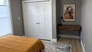Un dormitorio con una cama, un armario, un escritorio, un cartel y una ventana.