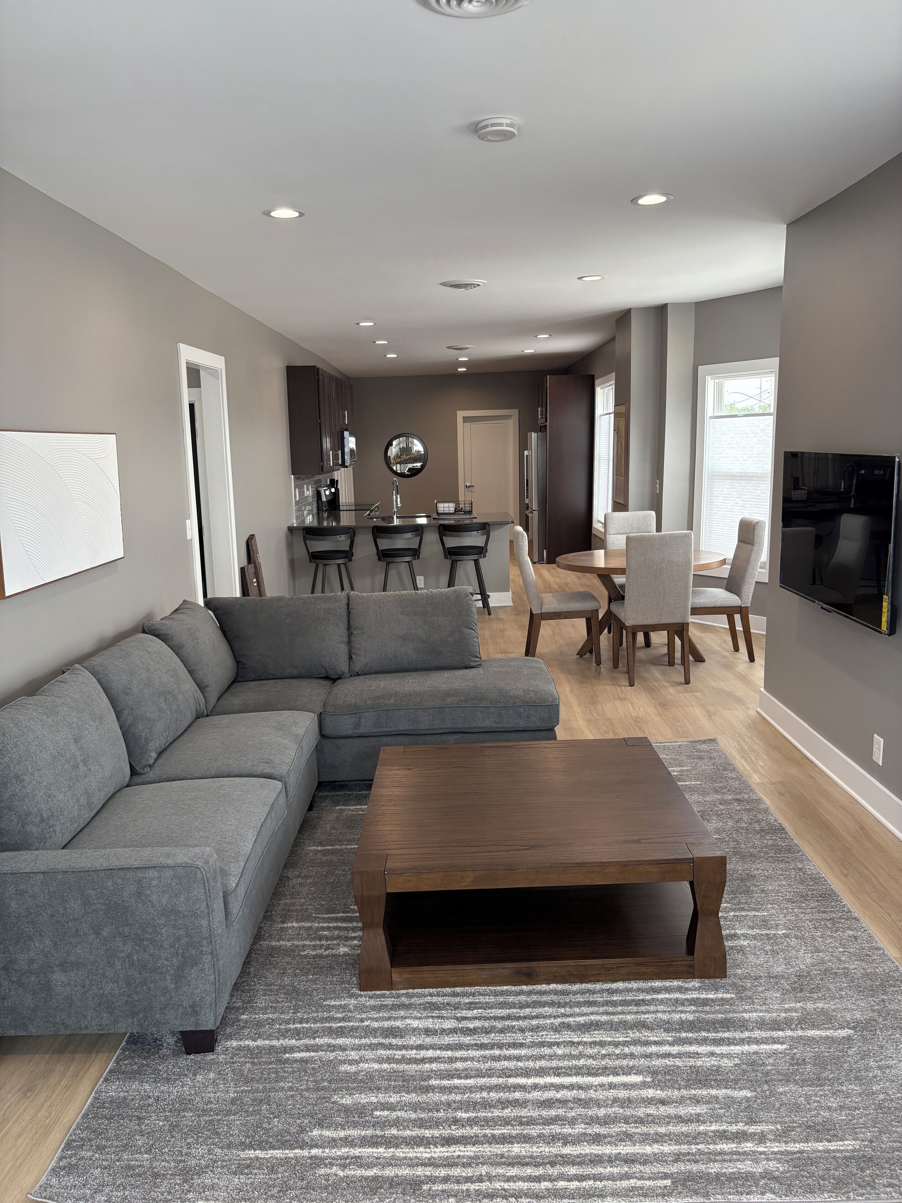 A modern living room with a sectional sofa, a coffee table, and a dining area with a table and chairs.