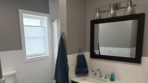 Un baño con inodoro blanco, lavamanos con espejo y zona de ducha con cortina.
