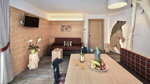 A cozy room with a wooden wall, a sofa, a dining table with fruit, and a mounted television. - Apartment 'Ban Rutzner Brixen' with Mountain View, Shared Terrace and Wi-Fi (SantʼAndrea in Monte)