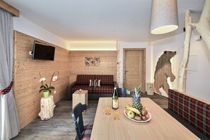 Une pièce chaleureuse avec un mur en bois, un canapé, une table à manger avec des fruits et un téléviseur fixé au mur.
