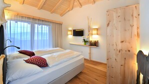 A bedroom with a bed, a TV, a wooden ceiling, and a window with curtains. - Apartment 'Ban Rutzner Brixen' with Mountain View, Shared Terrace and Wi-Fi (SantʼAndrea in Monte)