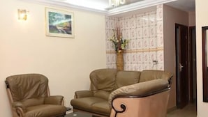Een woonkamer met twee beige fauteuils, een zwarte salontafel en een kroonluchter.