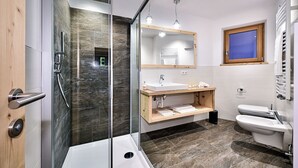 Ein modernes Badezimmer mit einer gläsernen Duschkabine, einem weißen Waschbecken und einer Holz-Kommode.
