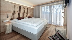 Ein Schlafzimmer mit einem großen Bett, Holzvertäfelung, einem Nachttisch mit Kerzen und einem Fenster mit durchsichtigen Vorhängen.