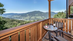 Ein Holzbalkon mit Tisch und Stühlen, der auf eine Berglandschaft blickt.