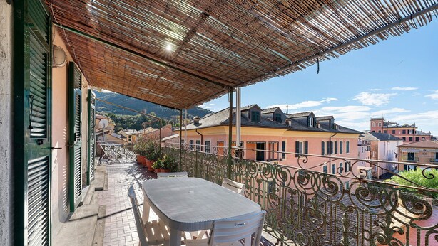 A balcony with a table and chairs, a metal railing, and a view of buildings and mountains. - Apartment 'Casa Terrazza Marino' with Private Terrace and Wi-Fi (Levanto)