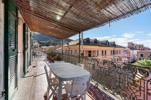 Ein Balkon mit Tisch und Stühlen, einem Metallgeländer und Blick auf Gebäude und Berge.