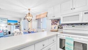 A kitchen with white cabinets, a microwave, an oven, and a dining area with a white table and chairs. - 🏖️BeachFront-2 Pools-Great Location-Pinnacle Port PH36🏖️ (Panama City Beach)