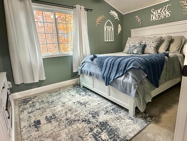 A bedroom with a bed, a window with curtains, a rug, and wall decorations.