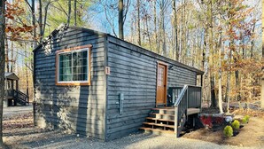 A small cabin with a wooden exterior, a front door, and a set of stairs leading to a porch. - Hidden Oaks | The Cottage | Unit 1 (Birch Run Township)