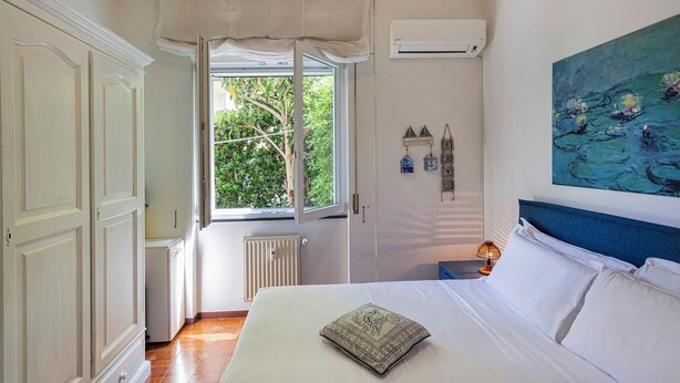 A bedroom with a bed, a window with curtains, an air conditioner, a radiator, and a painting on the wall. - Relax Apartment with Parking by Wonderful Italy (Santa Margherita Ligure)