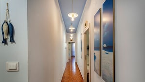 A hallway with a wooden floor, white walls, and a ceiling with pendant lights. There are framed artworks on the walls and a door at the end. - Relax Apartment with Parking by Wonderful Italy (Santa Margherita Ligure)